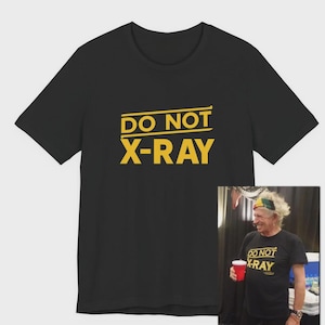 Könnte beinhalten: Schwarzes T-Shirt mit dem gelben Text "DO NOT X-RAY". Das Bild enthält auch ein kleineres Foto einer Person, die das gleiche T-Shirt trägt. Das T-Shirt hat einen Rundhalsausschnitt.