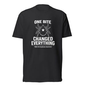 Puede incluir: Camiseta negra con texto blanco y un gráfico de garrapata. El texto dice "ONE BITE CHANGED EVERYTHING" con "Alpha-Gal Syndrome Awareness" debajo. El diseño presenta una garrapata con una estrella en el centro.