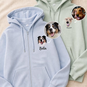 Puede incluir: Una sudadera con cremallera azul claro con el bordado de un perro llamado Bella y una sudadera con cremallera verde salvia con el bordado de un perro llamado River, cada una con una foto circular correspondiente del perro real.