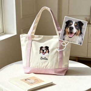 May include: A cream-colored canvas tote bag featuring a pink and white gingham pattern on the base and handles. The bag displays an embroidered portrait of a tricolor dog with the name Bella stitched in black thread below the dog's image.