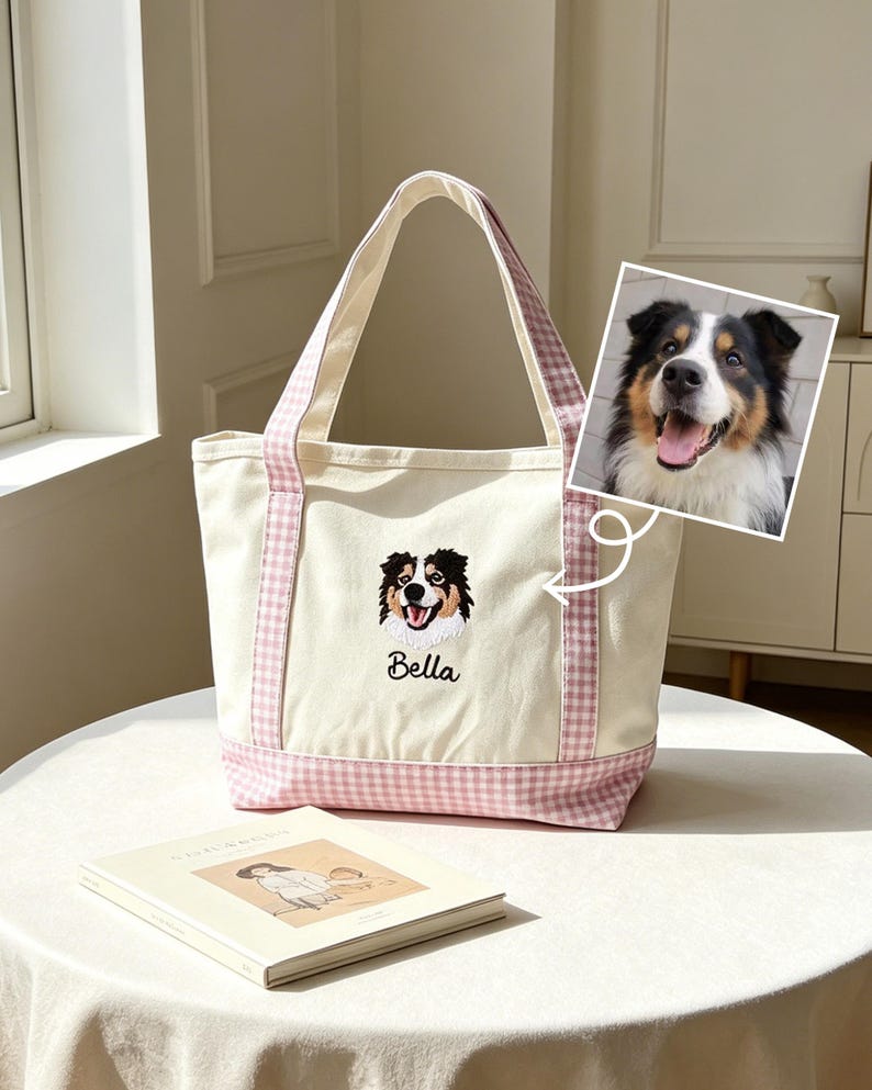 May include: A cream-colored canvas tote bag featuring a pink and white gingham pattern on the base and handles. The bag displays an embroidered portrait of a tricolor dog with the name Bella stitched in black thread below the dog's image.