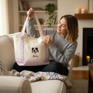 May include: A cream-colored canvas tote bag featuring a light pink and white gingham pattern on the base and handles. The bag displays an embroidered portrait of a tricolor dog above the name Bella stitched in black cursive lettering.