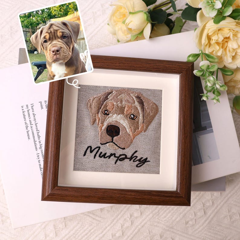 May include: A framed embroidered portrait of a dog with the name "Murphy" stitched below. The dog is brown and white, with a detailed embroidered design. A smaller photo of the dog is in the upper left corner.