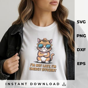 Puede incluir: Camiseta blanca con un gato de dibujos animados con gafas de sol y un sombrero. El gato es naranja y blanco con gafas de sol azules. El texto de la camiseta dice: "I'M NOT LAZY, I'M ENERGY EFFICIENT".