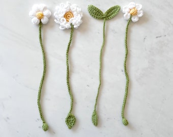 May include: Four crocheted daisy bookmarks with green stems and leaves. The daisies are white with yellow centers.