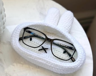 Może przedstawiać: Biały, szydełkowy organizer na okulary w kształcie królika z parą okularów w środku.