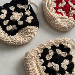 May include: Three crocheted bags with a granny square design. One bag is black and white, one is red and white, and one is black and white.
