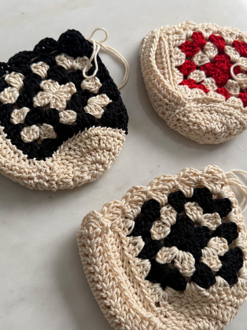 May include: Three crocheted bags with a granny square design. One bag is black and white, one is red and white, and one is black and white.