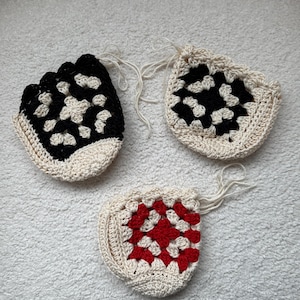 May include: Three crocheted granny square coasters in different color combinations. One is black and white, one is red and white, and one is black and white.