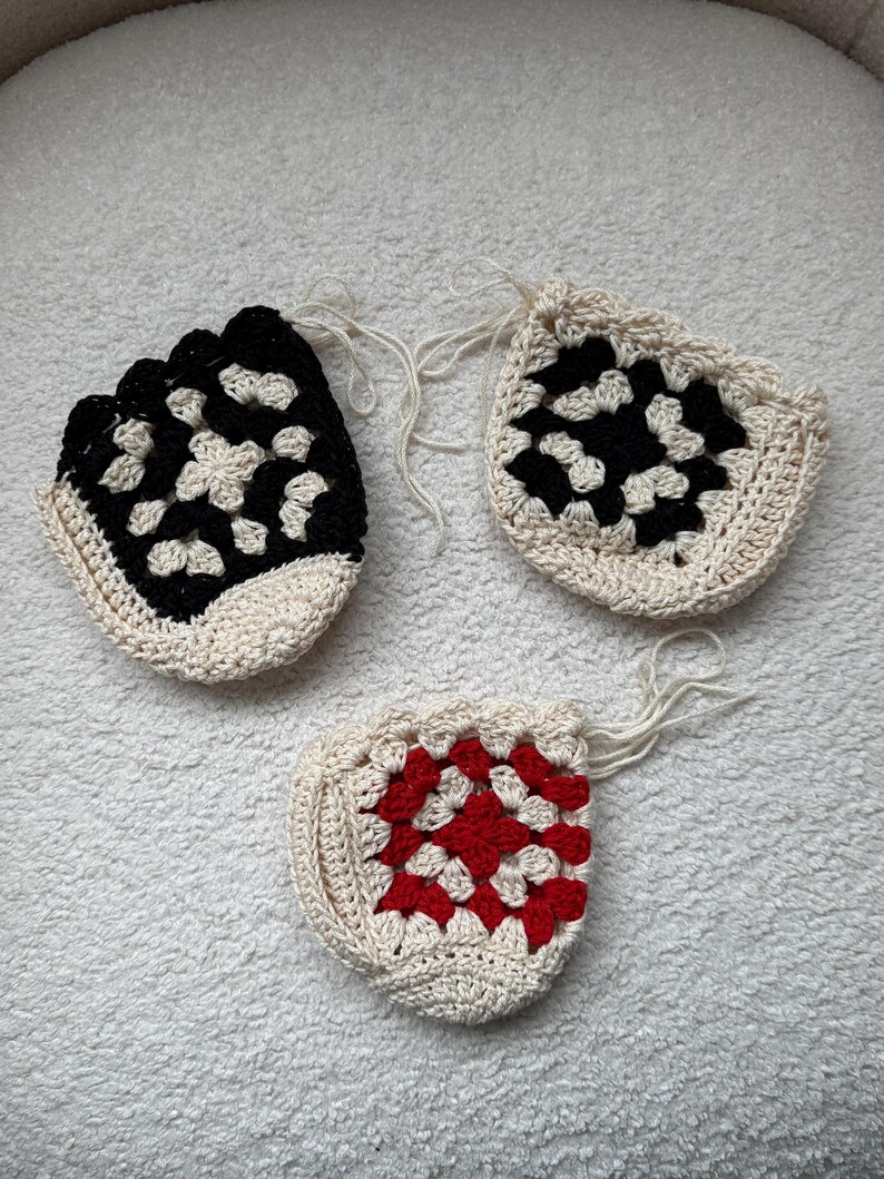 May include: Three crocheted granny square coasters in different color combinations. One is black and white, one is red and white, and one is black and white.