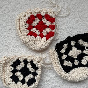 May include: Three crocheted granny squares in different color combinations. One square is white and red, one is white and black, and one is white and black.