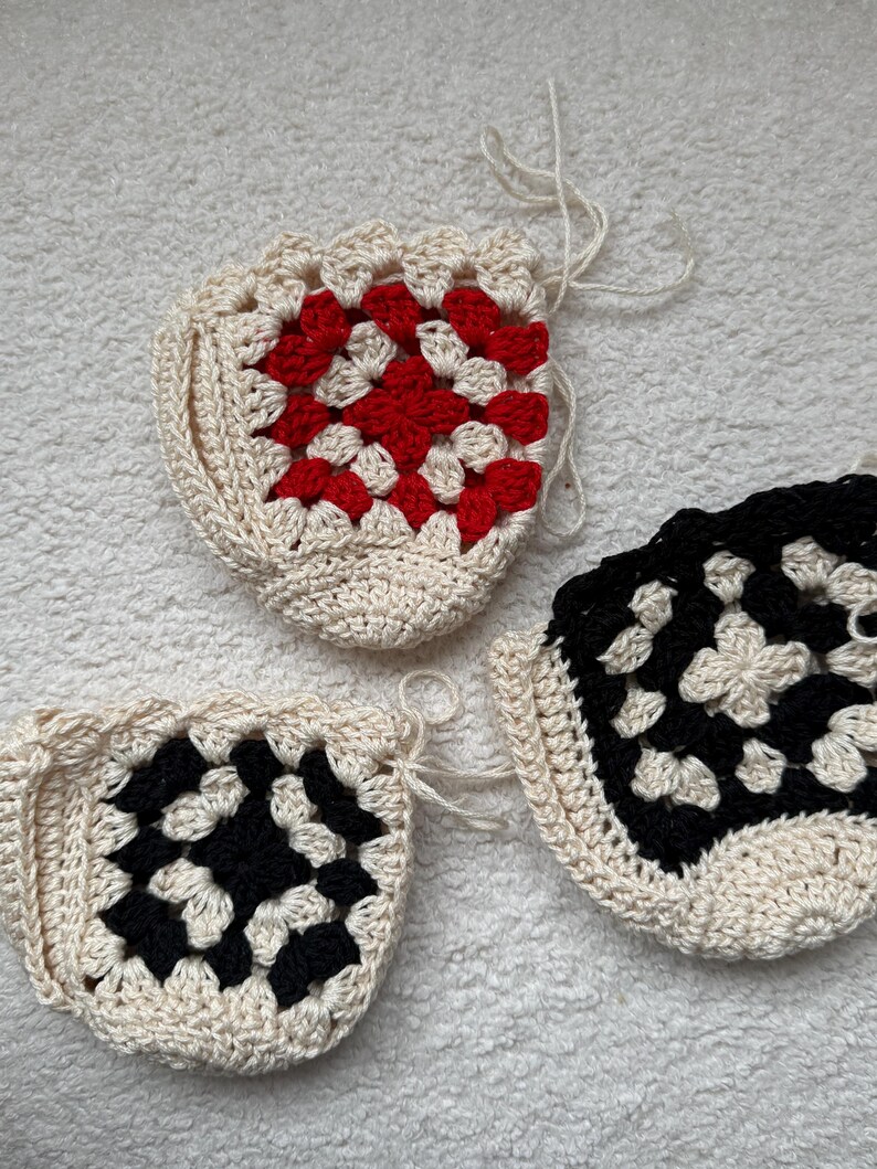 May include: Three crocheted granny squares in different color combinations. One square is white and red, one is white and black, and one is white and black.