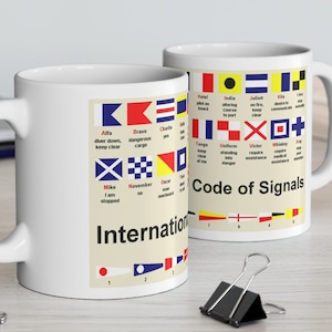May include: White ceramic mug featuring a colourful illustration of the International Code of Signals. The mug has a nautical theme with flags and the text "Code of Signals".