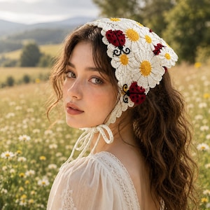 May include: A white crochet headscarf featuring a pattern of white daisies with yellow centers and red ladybug motifs with black spots. The headscarf has a scalloped edge and thin crocheted ties that fasten under the chin to secure the accessory.