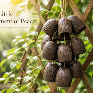May include: A cluster of brown, bell-shaped wind chimes hanging against a wooden trellis and lush green foliage. The chimes have a textured surface and are suspended by a woven cord. The text "A Little Moment of Peace" is visible.