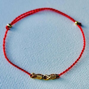 May include: Red string bracelet with three gold-coloured beads. The bracelet is made of a thin, bright red cord and features three decorative gold-toned beads in the centre. The bracelet is designed to be adjustable.