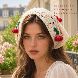 May include: A cream-colored crochet headscarf featuring small red cherry appliques with green leaves. The fabric has an intricate openwork pattern. The text "Handmade for Slow Days & Everyday Beauty" is printed in the upper right corner of the image.