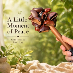 May include: A brown percussion instrument with a wooden handle and several brown seed pods. The text "A Little Moment of Peace" and "Soft Sounds for Slow Living" are also visible. The background is a soft focus of green foliage.