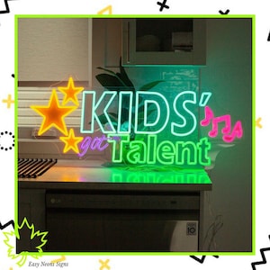 May include: A neon sign displaying "KIDS' got Talent" in green and white. The sign includes orange stars and pink musical notes. The sign is placed on a countertop, illuminated by a green neon glow.
