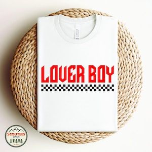 May include: White t-shirt with the text "LOVER BOY" in red letters and a black and white checkered pattern underneath.