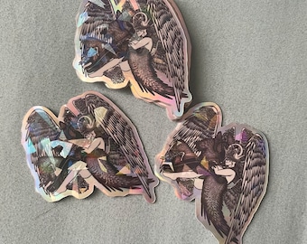 May include: Three iridescent stickers featuring a winged figure with a halo, holding a staff. The figure is depicted in a dark, detailed style with a holographic finish.