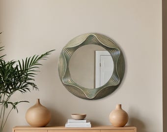 Pode incluir: Um espelho de parede redondo, decorativo, verde e dourado, com um design ondulado e orgânico. O espelho está pendurado em uma parede bege acima de uma mesa de consola de madeira com dois vasos e uma tigela no topo.
