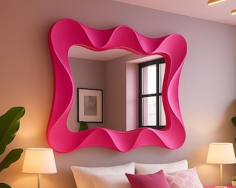 May include: A large, wavy-edged, hot pink mirror hangs on a neutral wall above a bed. The bedroom features a matching pink nightstand, a bed with pink bedding, and a window. A green plant is in the foreground.