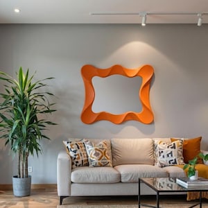 May include: A vibrant orange, organically shaped mirror adorns a grey wall above a beige sofa with patterned cushions. A tall green plant in a grey pot stands to the left. A black coffee table and rug complete the room.