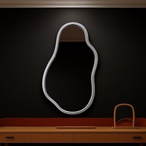 May include: An irregularly shaped mirror with a silver frame is mounted on a black wall. Beneath, a wooden vanity unit with drawers and a curved red top is seen. A small, arched wooden ornament rests on the vanity.