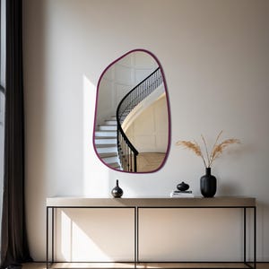 Irregular organic shaped wall mirror with dark wood frame hanging above a modern console table in a minimalist entryway with natural lighting