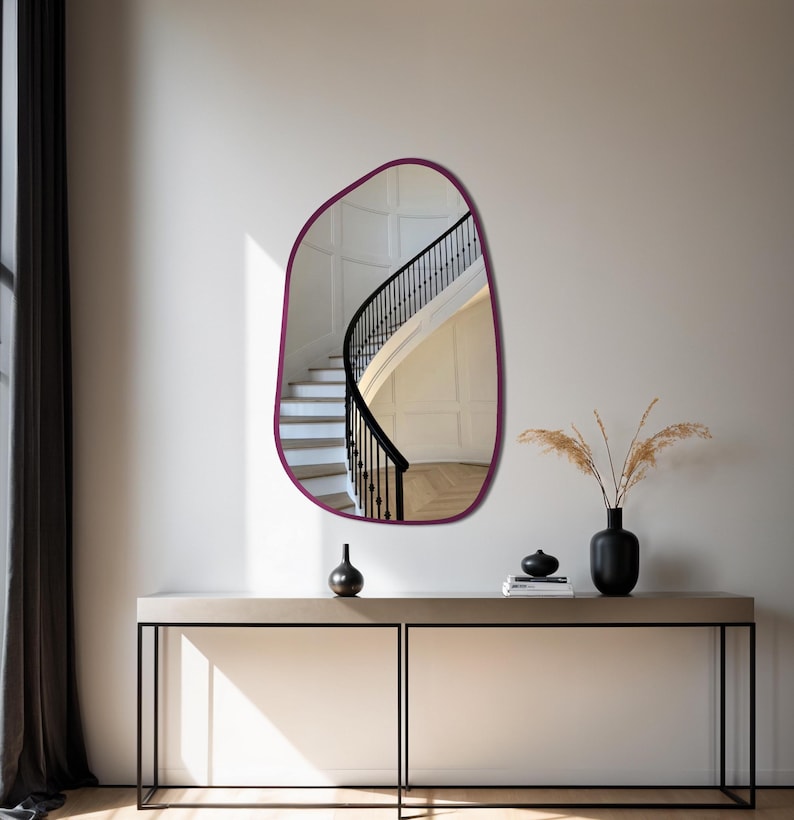 Irregular organic shaped wall mirror with dark wood frame hanging above a modern console table in a minimalist entryway with natural lighting