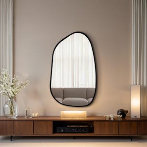 Large asymmetrical wall mirror with black frame above a walnut floating TV console in a modern minimalist living room