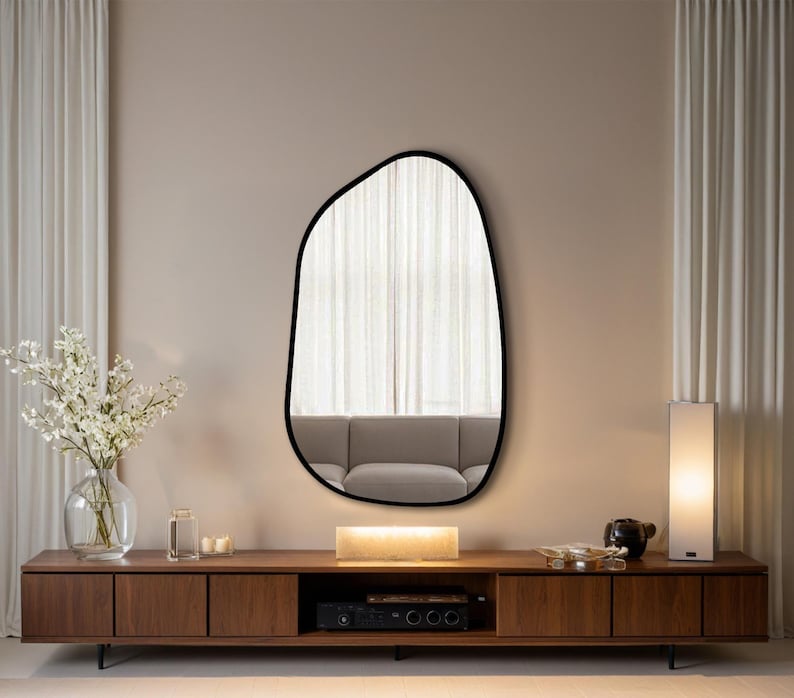 Large asymmetrical wall mirror with black frame above a walnut floating TV console in a modern minimalist living room