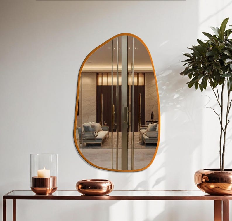 Bronze-colored sculptural wall mirror with soft, organic curves, mounted in a modern entryway with warm-toned copper accents and minimalist decor.