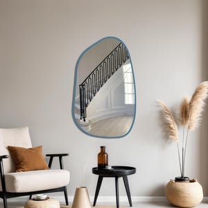 Blue framed asymmetrical wall mirror in a cozy boho living room with accent chair, pampas grass, and minimalist decor