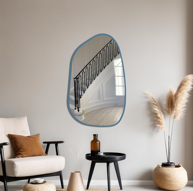 Blue framed asymmetrical wall mirror in a cozy boho living room with accent chair, pampas grass, and minimalist decor