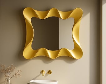 May include: A gold-colored, wavy-framed mirror hangs on a wall. The mirror has a rectangular shape with a unique, flowing design. The bathroom decor includes a white sink, gold fixtures, and a vase of dried flowers.