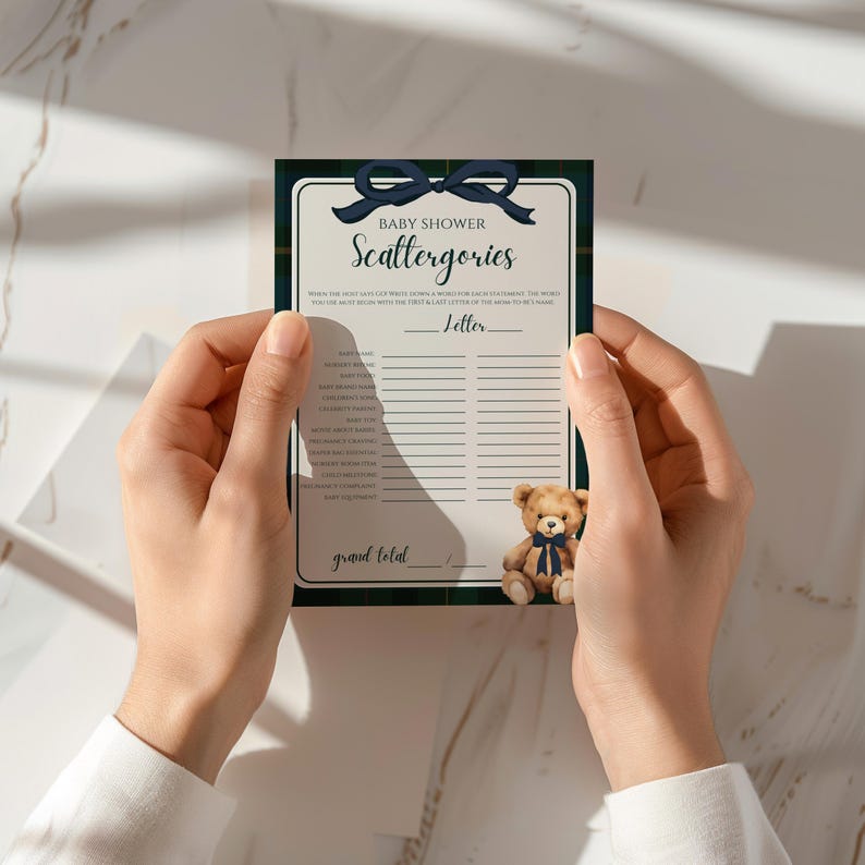 May include: A baby shower Scattergories game card with a navy blue bow and a teddy bear. The card has a green and navy plaid border and includes prompts for the game. The text "Baby Shower Scattergories" is at the top.