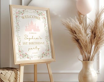May include: A welcome sign for a princess's 1st birthday party. The sign features a pink castle with a gold inscription that reads "Welcome to Princess Sophia's 1st Birthday Party". The sign is surrounded by a floral border with pink flowers and green leaves.