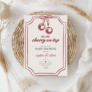Op de afbeelding: Een rode en witte babyborrel uitnodiging met een kers op de top ontwerp. De tekst luidt "Zij is de kers op de taart" en "U bent van harte welkom op onze babyborrel ter ere van Sophia & Oliver".