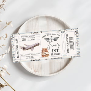 May include: A blue and white airplane ticket invitation with the text "Boarding Pass" and "Pack Your Bags For Jame's 1st Flight". The ticket has a vintage design with a small airplane, suitcases, and a barcode.
