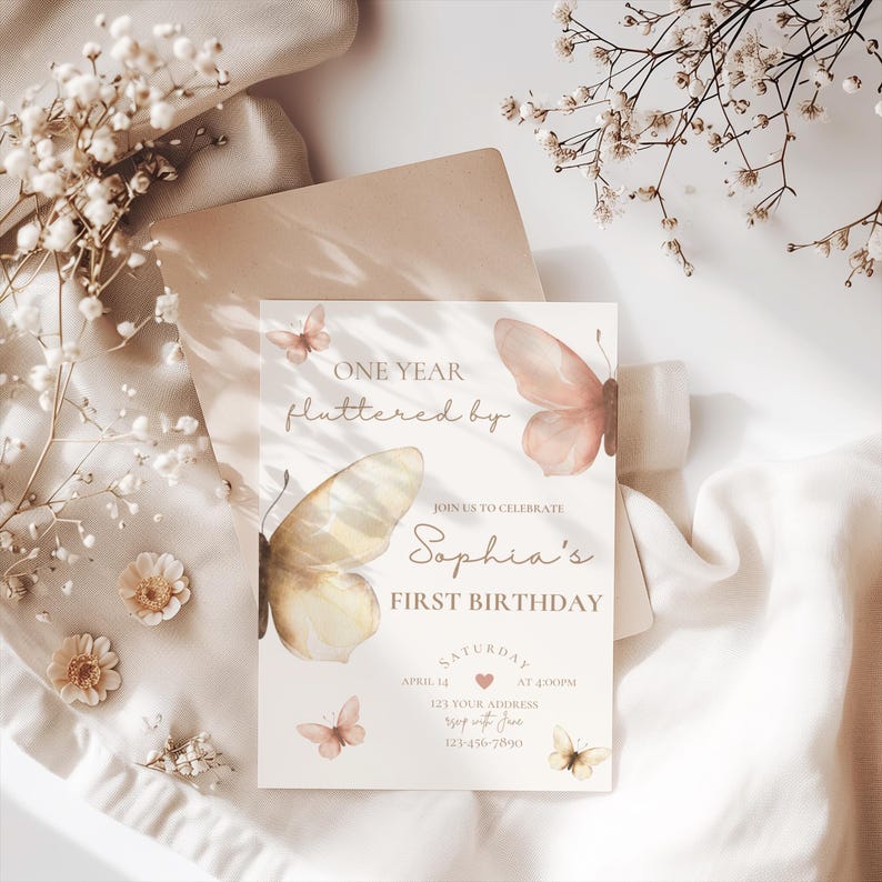 May include: A light beige invitation card with butterfly illustrations and the text "ONE YEAR fluttered by" and "Sophia's FIRST BIRTHDAY". The card includes details for a birthday celebration, with a soft, elegant design.