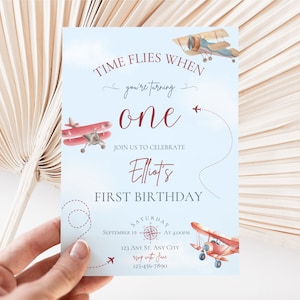 May include: A blue and white airplane themed first birthday invitation with red airplanes and the text "Time Flies When You're Turning One. Join Us To Celebrate Elliot's First Birthday. Saturday, September 19 at 4:00PM. 123 Any St. Any City. RSVP with Jane. 123-456-7890"