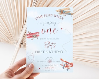 May include: A blue and white airplane themed first birthday invitation with red airplanes and the text "Time Flies When You're Turning One. Join Us To Celebrate Elliot's First Birthday. Saturday, September 19 at 4:00PM. 123 Any St. Any City. RSVP with Jane. 123-456-7890"