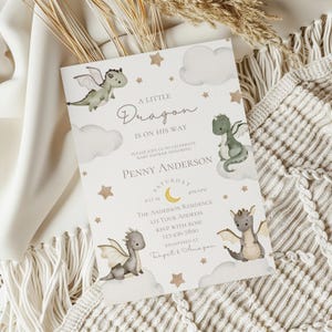 Op de afbeelding: Een rechthoekige uitnodigingskaart voor een babyshower met vier geïllustreerde draken, wolken en sterren. De tekst luidt: A LITTLE DRAGON IS ON HIS WAY, PLEASE JOIN US TO CELEBRATE BABY SHOWER HONORING PENNY ANDERSON, SATURDAY JULY 24, 4PM-6PM, THE ANDERSON RESIDENCE, 123 YOUR ADDRESS, RSVP WITH ROSE 123-456-7890, REGISTERED AT Target & Amazon.