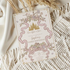 K&ouml;nnte beinhalten: Eine cremefarbene Einladung mit M&auml;rchenmotiv. Das Design zeigt ein goldenes Schloss, rosa B&auml;nder, florale Akzente und den Text "One Upon a time..." und "Sophia's Third Birthday". Schmetterlinge und dekorative Bord&uuml;ren runden das Design ab.