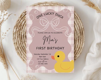 May include: A pink and white gingham patterned birthday invitation with the text "ONE LUCKY DUCK" and "Mia's FIRST BIRTHDAY". A yellow rubber duck illustration is on the bottom right. The invitation is on a woven placemat.