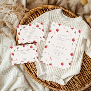 Puede incluir: Un juego de invitaciones para baby shower con temática de fresas. El juego incluye tarjetas de invitación, una tarjeta de rifa de pañales y una tarjeta de "Libros para bebé". Las tarjetas están decoradas con fresas rojas y lazos rosas. También hay un body blanco.