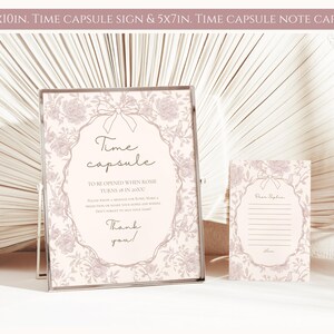 May include: A pink and white time capsule sign with a floral design and the text "Time capsule to be opened when Rosie turns 18 in 20XX". The sign is 8x10 inches. A smaller pink and white note card with a floral design and the text "Dear Rosie" is 5x7 inches.