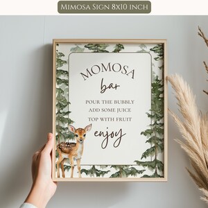 May include: A rectangular 8x10 inch sign in a light wood frame featuring a watercolor forest border with green pine trees and a small brown fawn. The text reads: MOMOSA bar, POUR THE BUBBLY, ADD SOME JUICE, TOP WITH FRUIT, enjoy.